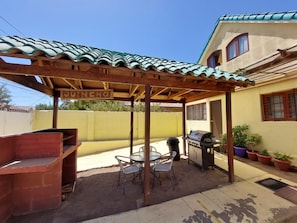 Un patio con pérgola, mobiliario exterior, una parrilla y un cartel que dice 'QUINCHO'.