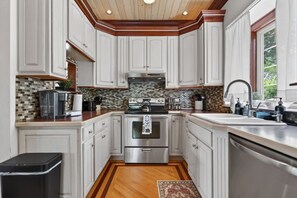 A kitchen with white cabinetry, a stainless steel stove, and a wooden floor. - The April Inn - A Historic Victorian Lakehouse (Spring Grove)