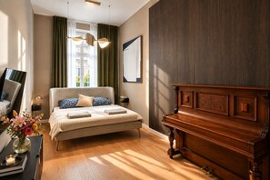 A bedroom with a bed, a wooden piano, a nightstand, a mirror, and a window with curtains. - Elegant Prague Apt•Wenceslas Square• City Center (Praha)