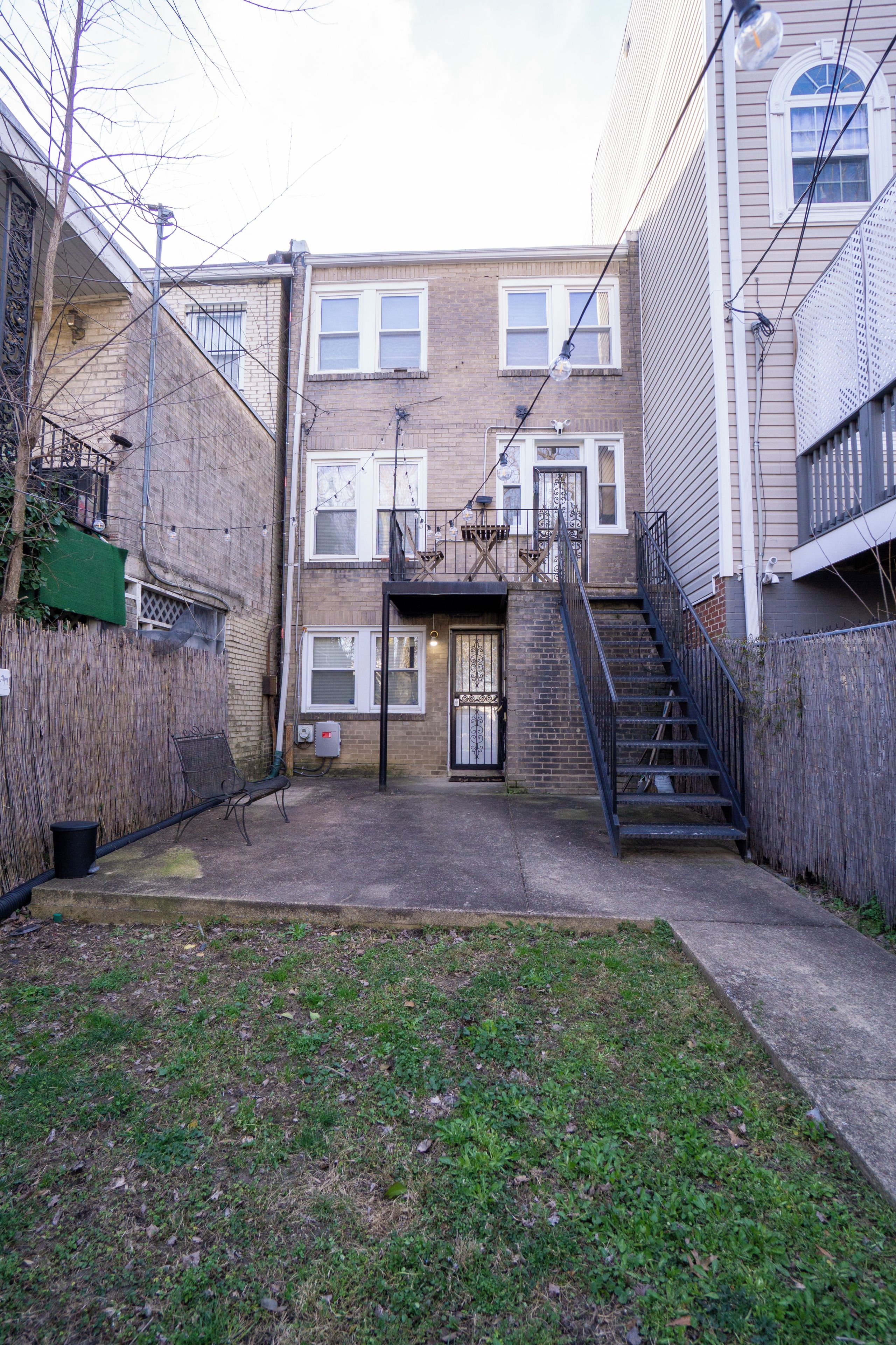 A residential building with a brick facade, multiple windows, a visible door, and a staircase leading to an upper level.