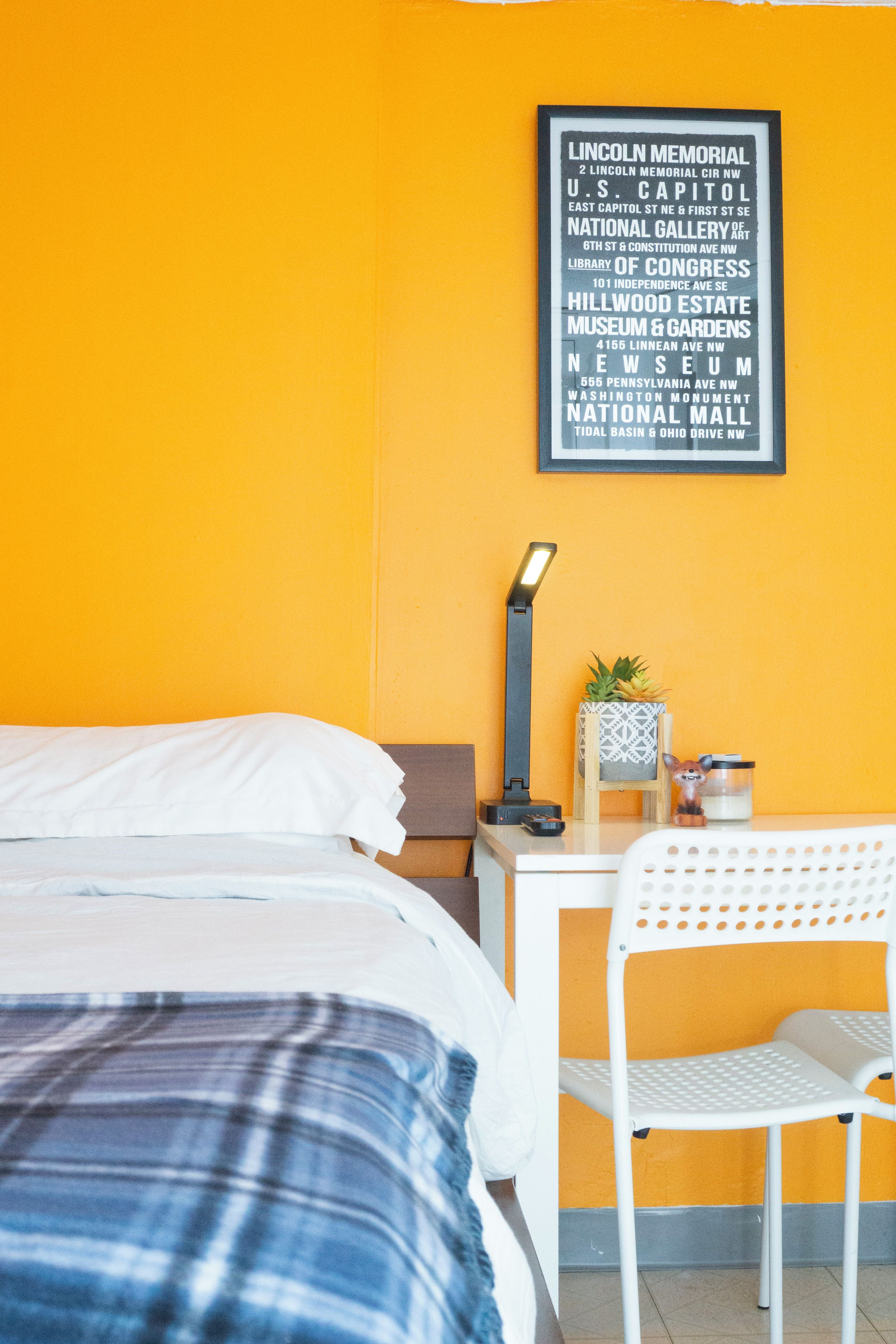 A hotel room with a bed, a desk, a chair, and a wall with a framed sign listing nearby attractions.