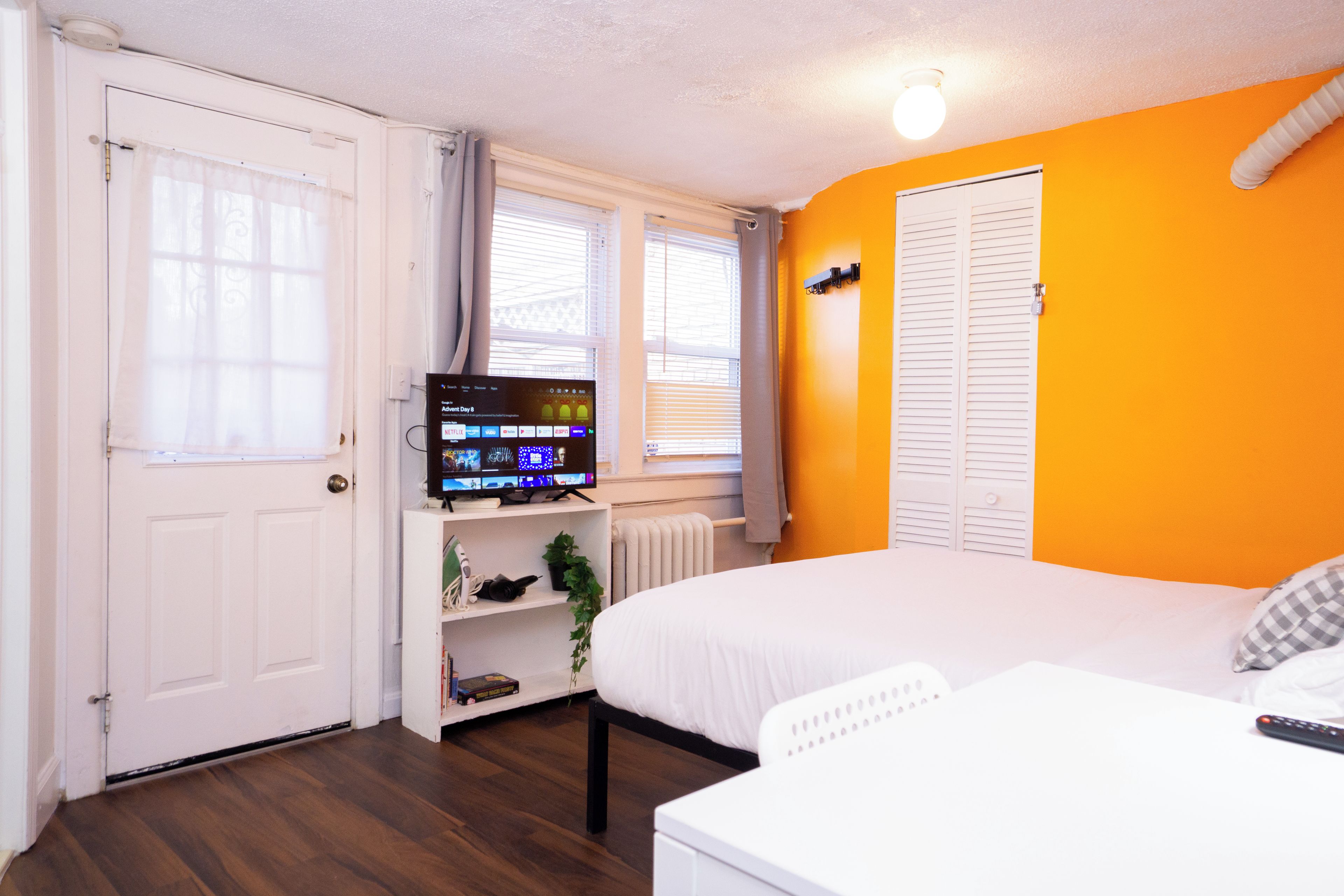 Une chambre à coucher avec un lit, une télévision, une étagère avec des objets et une fenêtre.