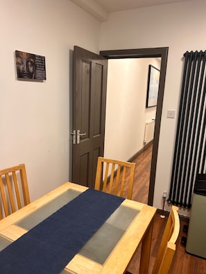 Une pièce comprenant une table à manger en bois, deux chaises, une porte, un radiateur et un tableau encadré accroché au mur.