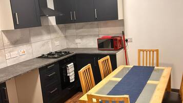 Una cocina compacta con estufa a gas, microondas y una mesa de comedor con sillas.