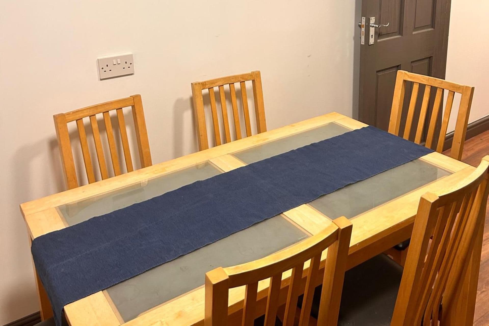 A dining table with a glass top and a blue table runner, surrounded by wooden chairs.
