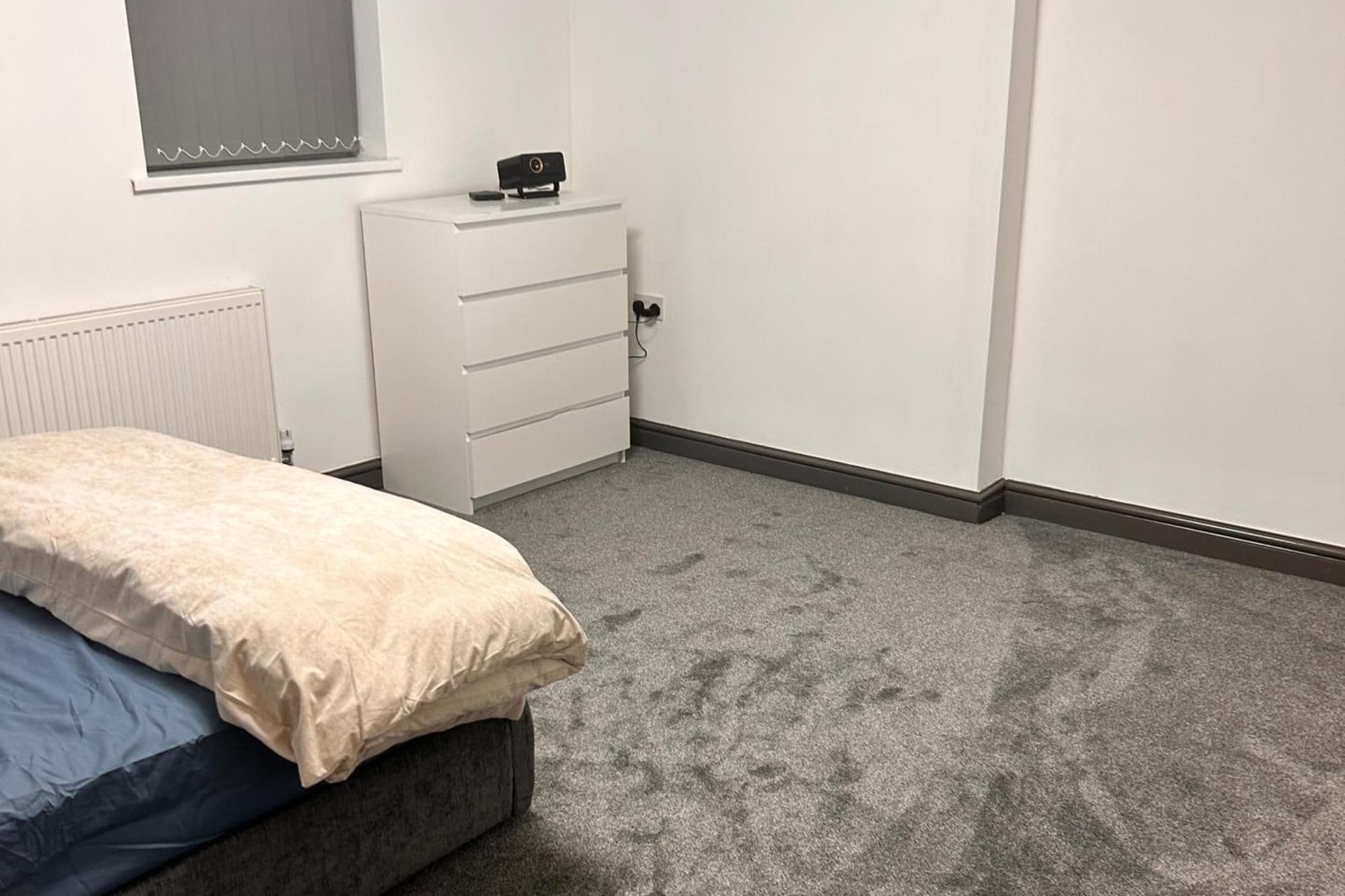 A bedroom with a bed, a dresser, a radiator, and a window with blinds.