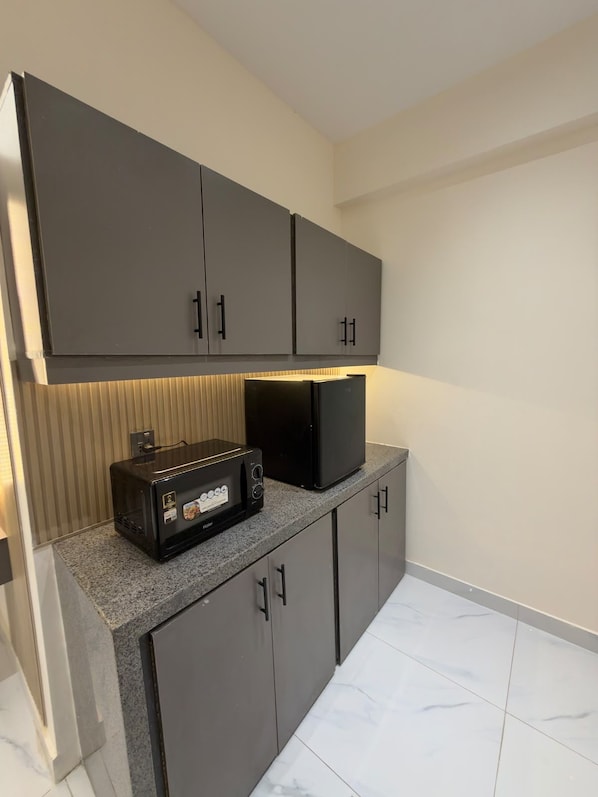 Cozinha compacta com armários cinza, micro-ondas embutido e torradeira.