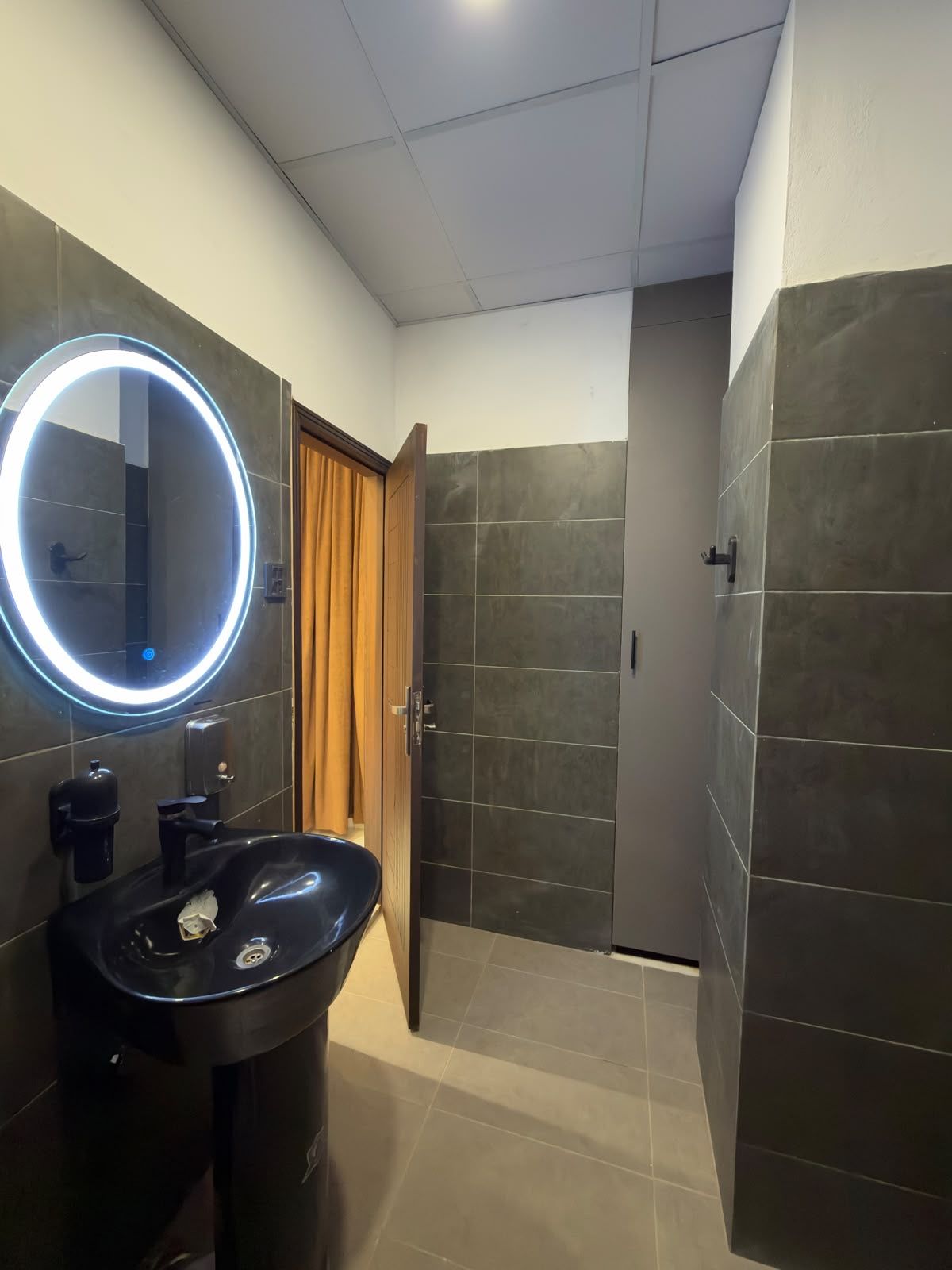 Une salle de bain avec un miroir rond, un lavabo noir et un espace douche.