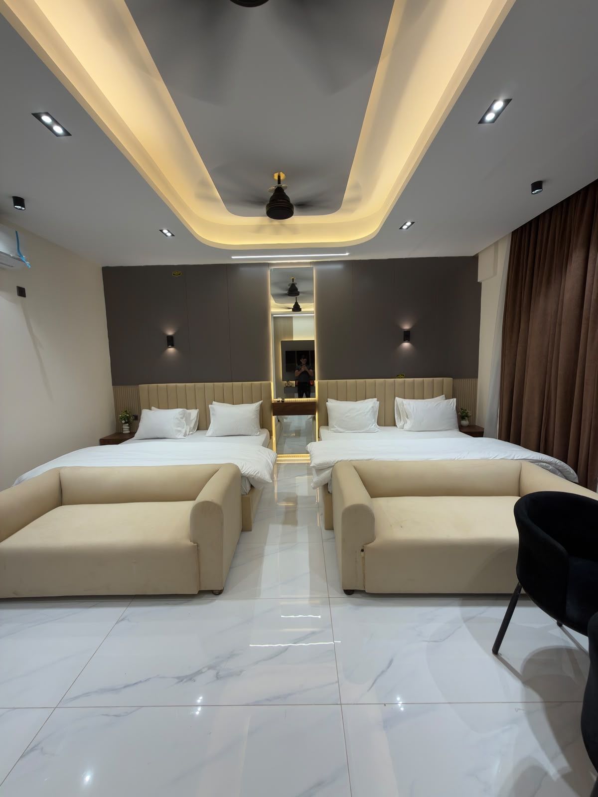 Ein modernes Hotelzimmer mit einem zentralen Bett, zwei Sofas, einem Deckenventilator und Einbauleuchten.