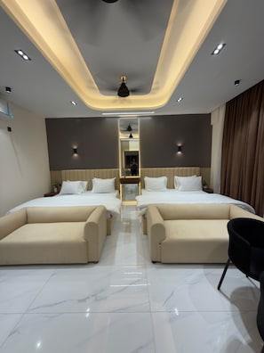 Quarto de hotel moderno com cama central, dois sofás, ventoinha no teto e iluminação embutida.
