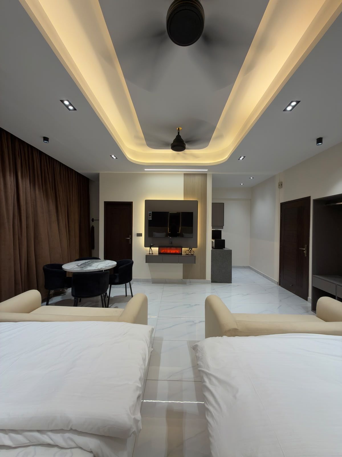Une chambre d’hôtel moderne dotée d’une télévision à écran plat, d’une cheminée, d’un coin repas avec une table et des chaises, et d’un grand lit.