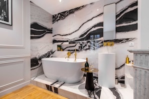 Ein modernes Badezimmer mit einer freistehenden Badewanne, Marmorwänden und einem großen Spiegel.