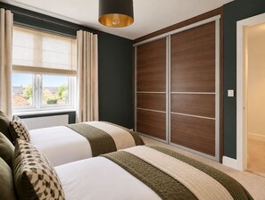 Une chambre avec deux lits, une grande fenêtre avec des rideaux, une armoire et un luminaire suspendu.