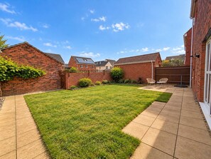 Un jardin arrière d’une maison, avec une pelouse, un espace patio et un mur en briques.