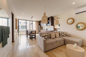 A modern living room with a sectional sofa, dining area, and kitchen in the background. - Elegant 3BR Penthouse with Private Rooftop Pool (Tulum)