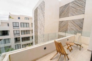 A balcony with two wooden chairs, a glass railing, and a view of a multi-story building. - Elegant 3BR Penthouse with Private Rooftop Pool (Tulum)