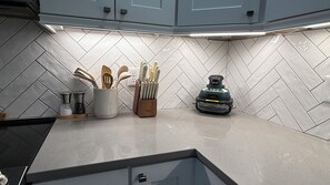 Ett kök med ett stänkskydd av fiskbensmönstrade kakelplattor, ett knivställ, en kryddhylla och en kaffemaskin.