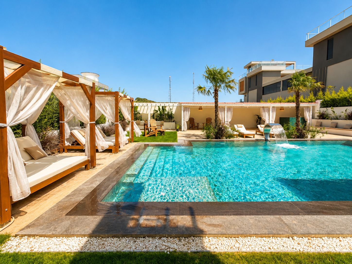 A swimming pool with a clear blue water feature, surrounded by lounge chairs and a covered seating area.