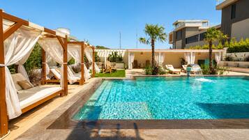 A swimming pool with a clear blue water feature, surrounded by lounge chairs and a covered seating area.