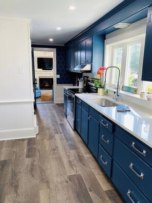 Une cuisine moderne avec des meubles de couleur bleu foncé, un plan de travail blanc et une fenêtre donnant sur un paysage agréable.