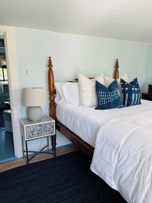 Quarto de hotel com cama, mesa de cabeceira, luminária e termostato fixado na parede.