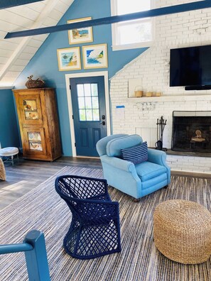A room with a blue sofa, a wicker chair, a fireplace, and a wooden cabinet with artwork. - Marion Renovated Home-Outdoor-Walk Tabor-Village (Marion)