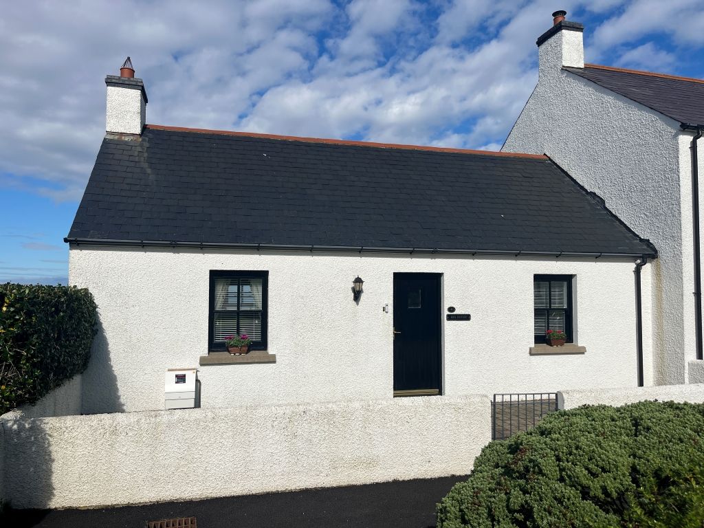 A white building with a dark roof, a black door, and two windows with shutters.