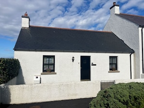 A white building with a dark roof, a black door, and two windows with shutters. - Cosy Cottage on the North Antrim Coast of Northern Ireland near Ballintoy. (Ballintoy)