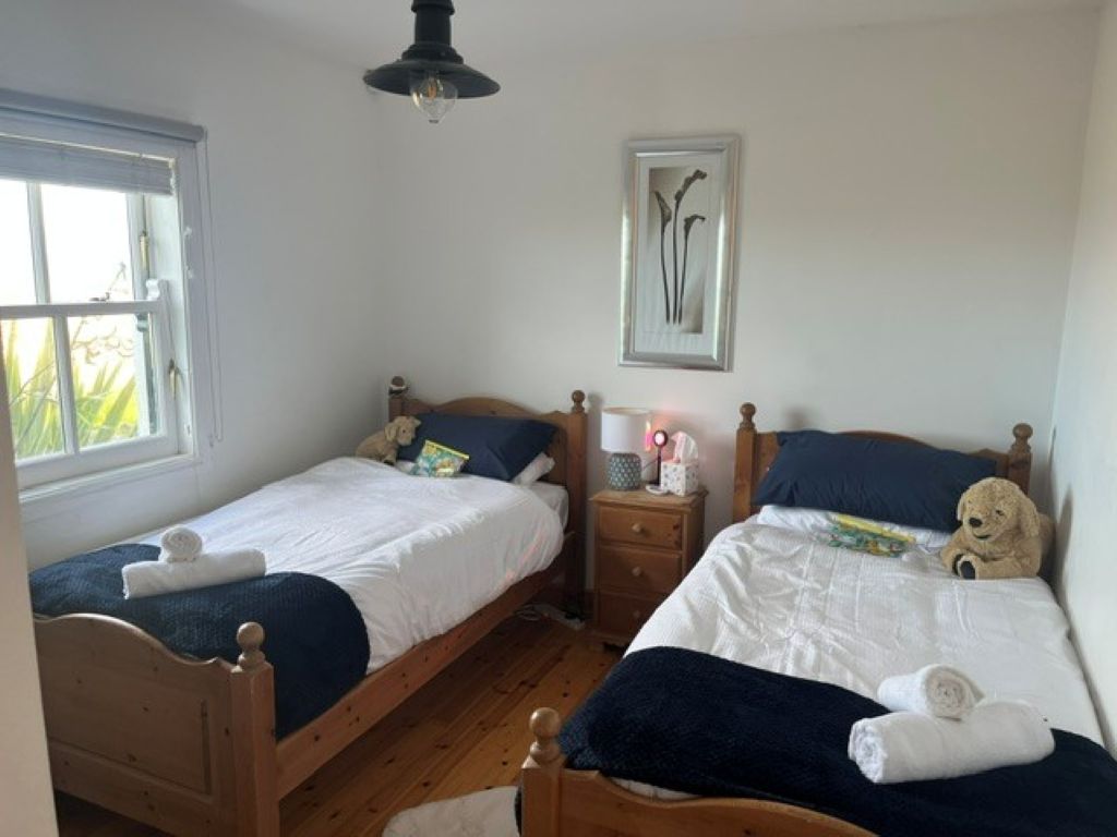 A bedroom with two wooden beds, a nightstand, a framed picture on the wall, and a window with curtains.