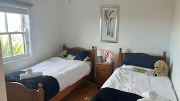 A bedroom with two wooden beds, a nightstand, a framed picture on the wall, and a window with curtains.