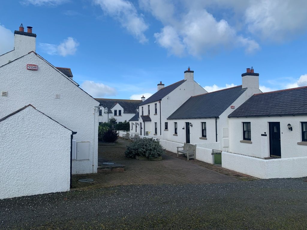 A row of white buildings with dark roofs, a gravel path, and a bench.