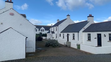 A row of white buildings with dark roofs, a gravel path, and a bench.