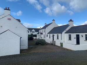 A row of white buildings with dark roofs, a gravel path, and a bench.