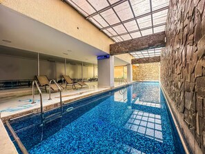 An indoor swimming pool with clear blue water, lounge chairs, and a stone wall. - Quito 2BR with Heated Pool & Gym Sleeps 4 Walk to Quicentro &  Estadio Atahualpa (Quito)