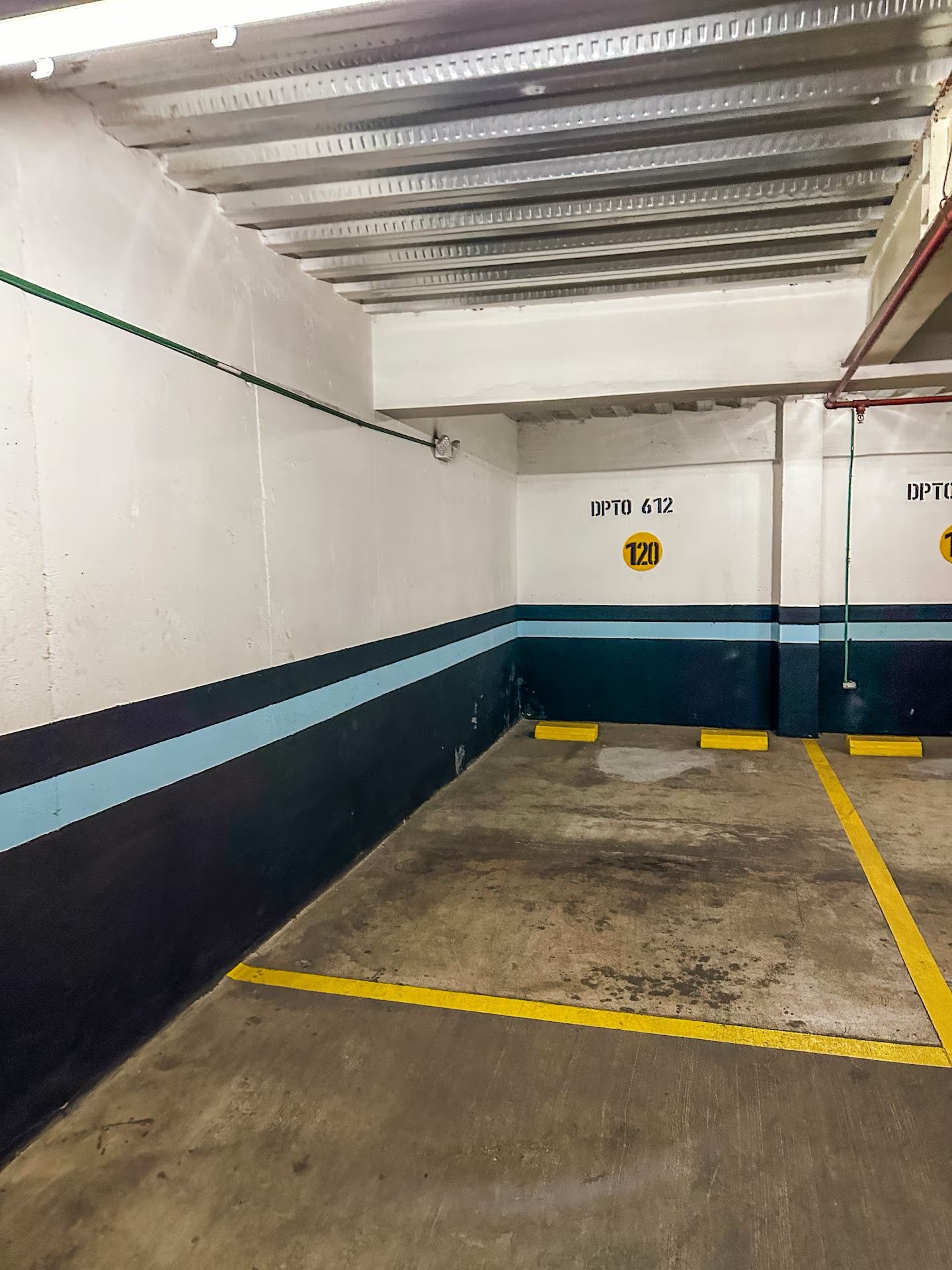 A parking garage with concrete floors, white walls with blue stripes, and yellow parking lines.