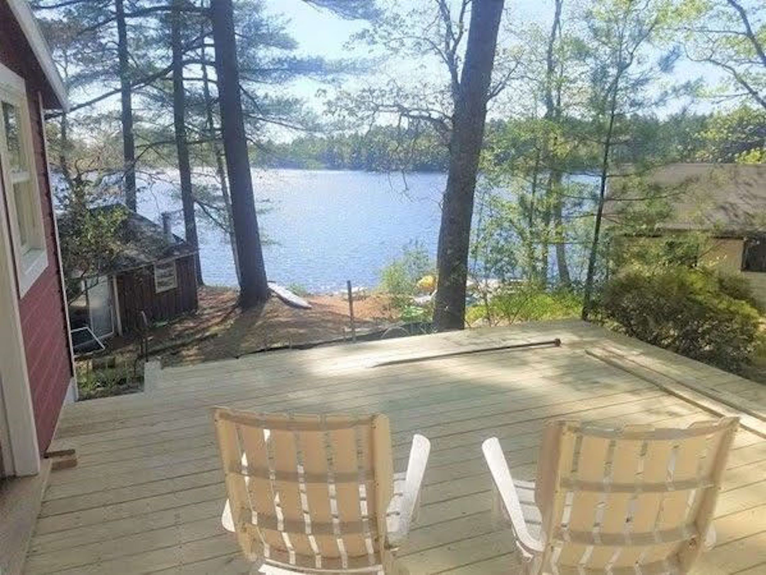 A deck with two Adirondack chairs overlooking a lake.