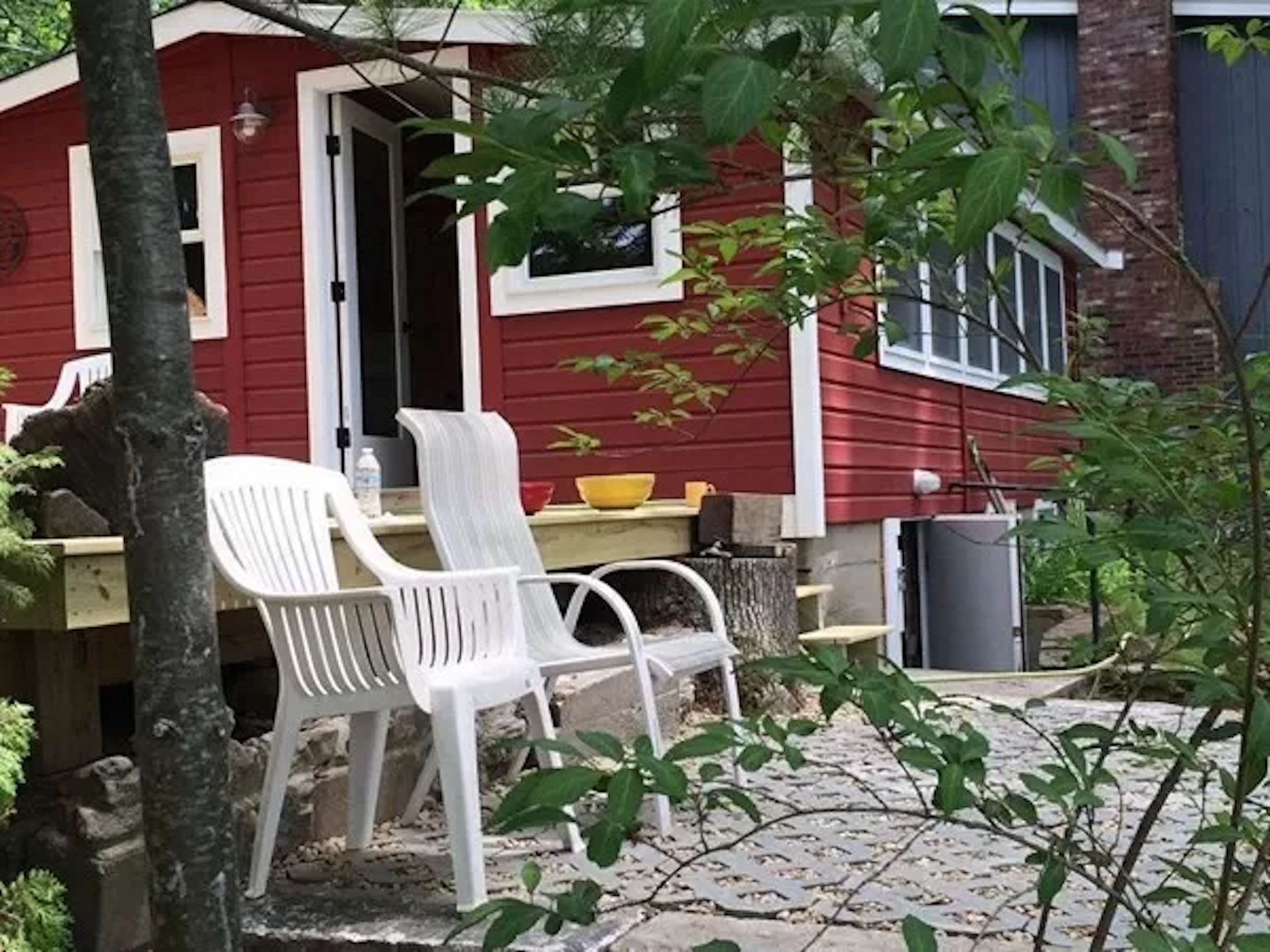 A red building with a white door, outdoor seating with white chairs, and a small table with a yellow bowl.