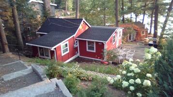 A red house with a black roof, surrounded by trees and a garden with white flowers.