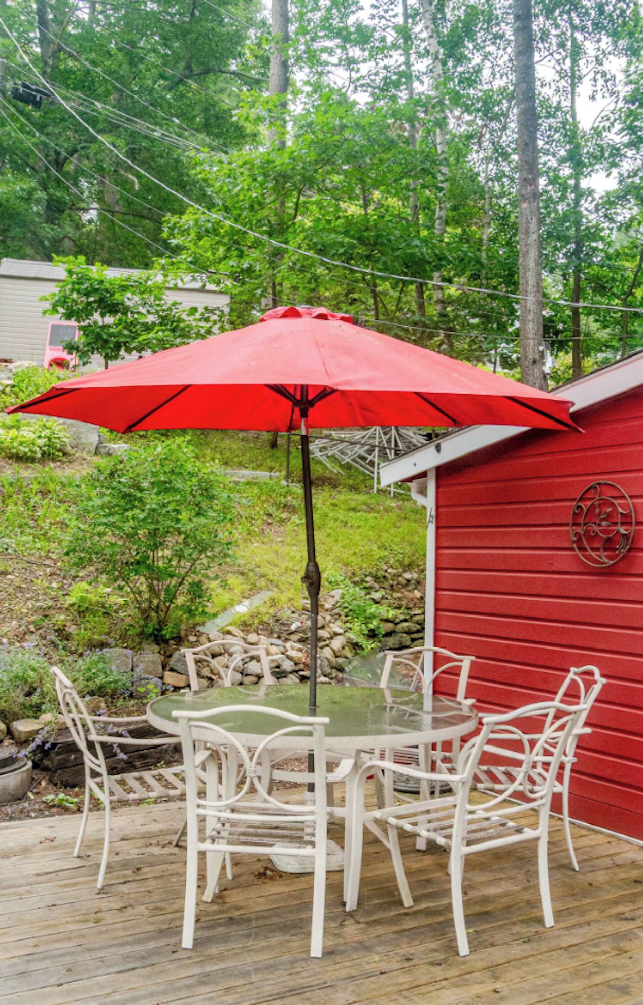 A red wooden deck with a table and chairs, an umbrella, and a red building in the background.