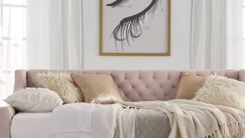 A pink sofa with a quilted cover, multiple pillows, and a framed artwork above.