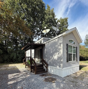 A small, single-story cabin with a porch and satellite dishes.