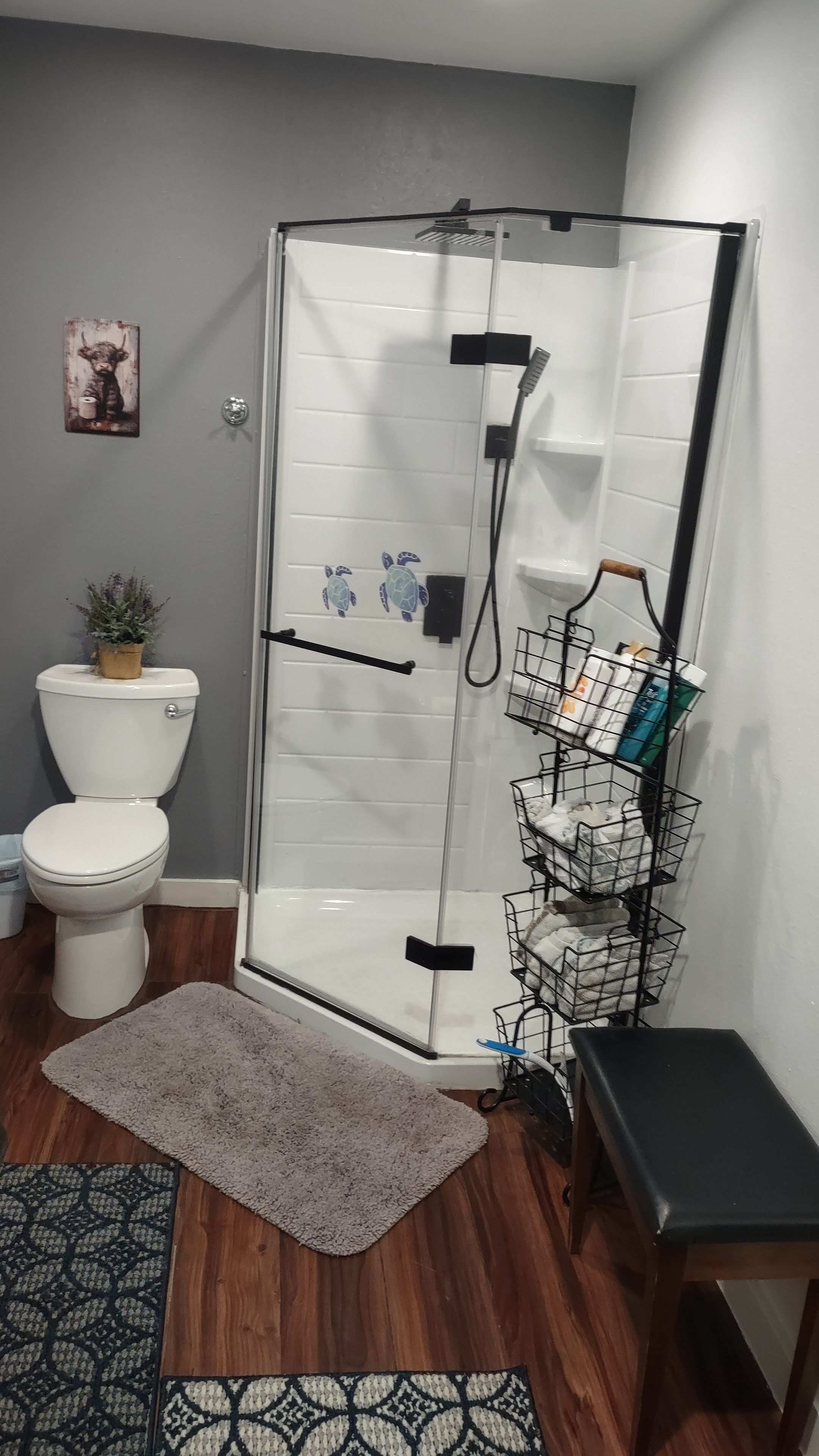 A bathroom with a glass-enclosed shower, a toilet, a sink, and a small bench.