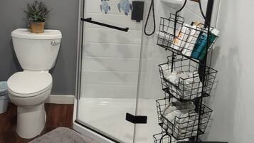A bathroom with a glass-enclosed shower, a toilet, a sink, and a small bench.