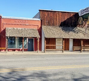 Une rue bordée d’un immeuble en briques rouges, d’une structure en bois avec une enseigne et d’un banc.