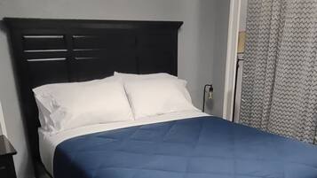 A bed with a dark headboard, white pillows, and a blue bedspread in a room with a patterned carpet.