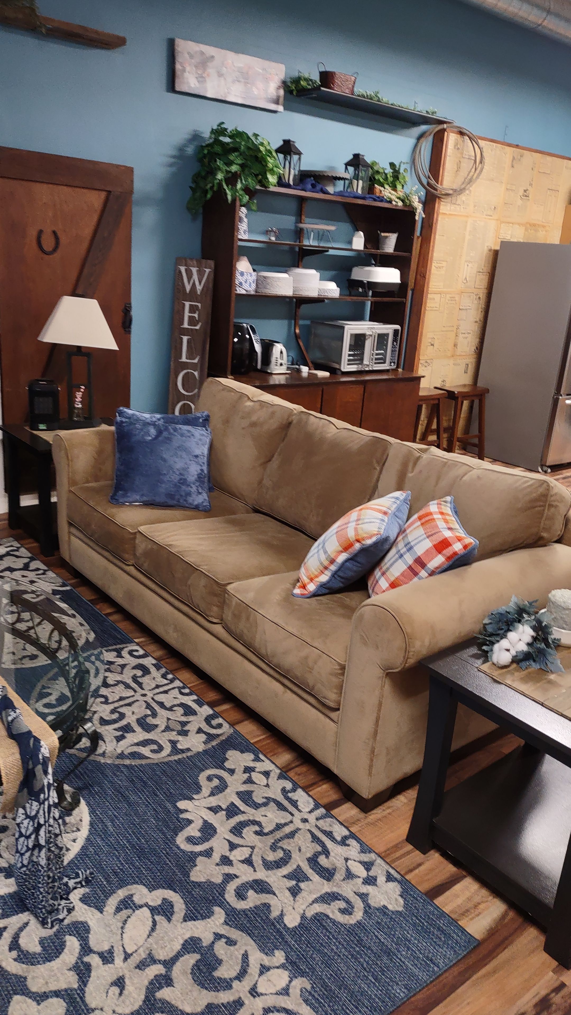 A living room with a beige sofa, patterned rug, and a 'WELCOME' sign.