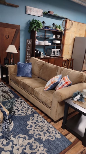 A living room with a beige sofa, patterned rug, and a 'WELCOME' sign.