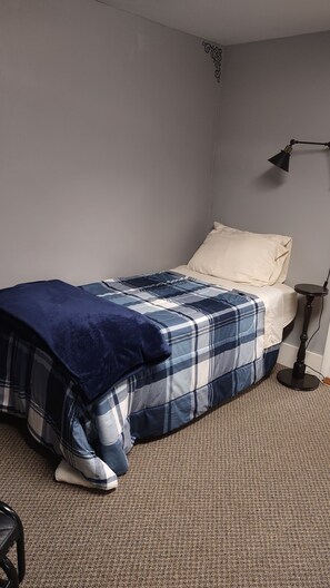 Une chambre à coucher avec un lit, une table de chevet, une lampe et un sol recouvert d’une moquette.