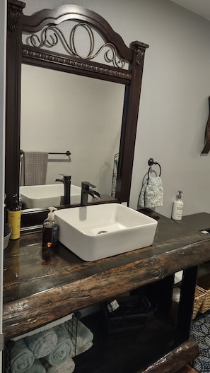 Un baño con lavamanos blanco, tocador de madera oscura y un espejo grande con detalles ornamentales.