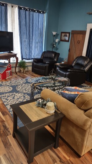 Un salon comprenant un canapé, deux fauteuils, une table basse, un téléviseur et un tapis à motifs.